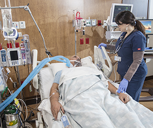 Proveedor de atención médica atendiendo a un hombre intubado en una cama de la unidad de cuidados intensivos.